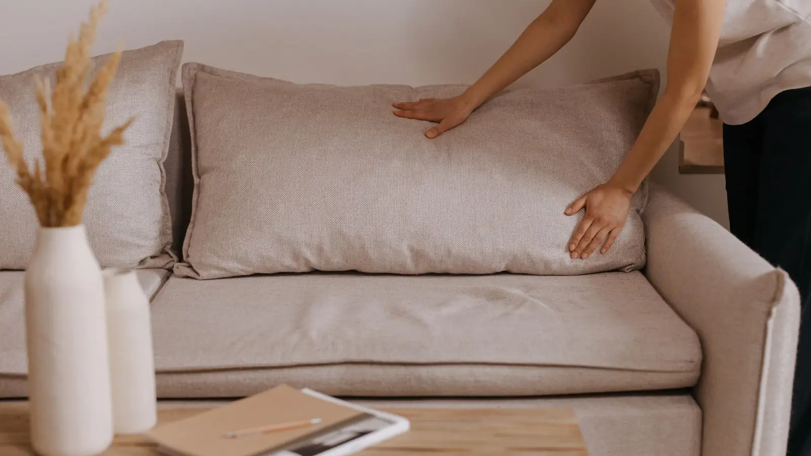 Cropped hands plumping a cushion on a pale beige sofa